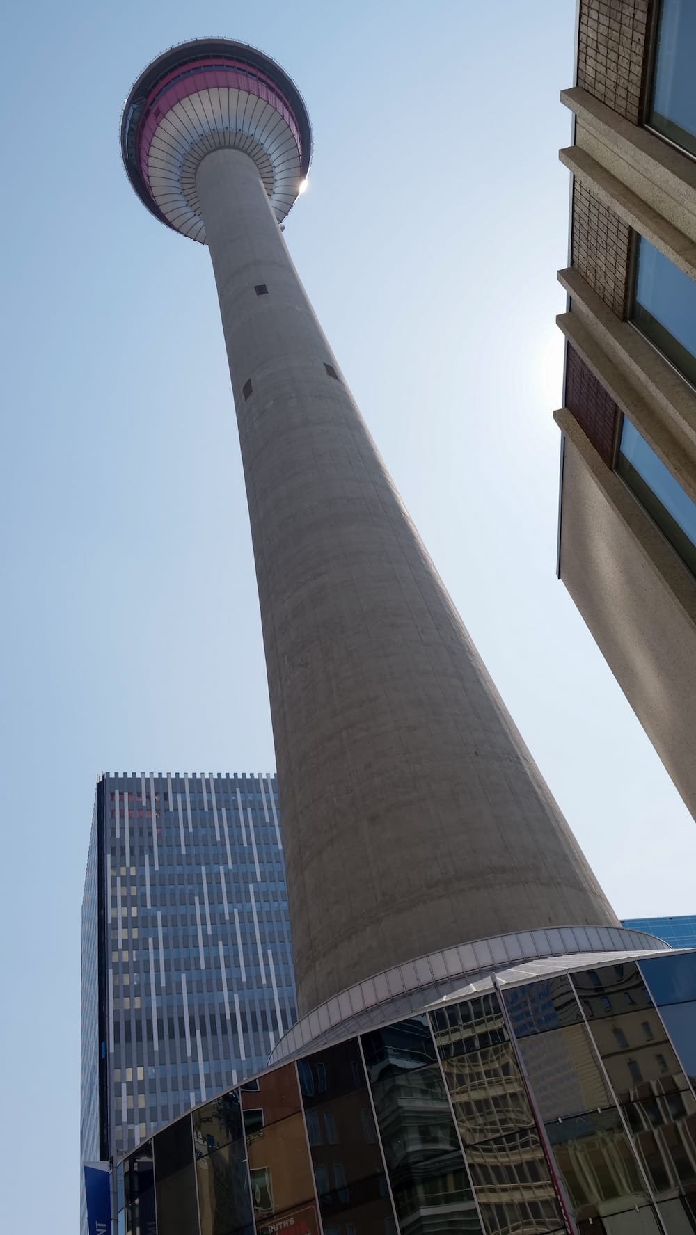 Vista en contrapicado de Calgary Tower desde la calle en Calgary, Alberta, Canadá, bajo un cielo azul Vista desde la calle y en contrapicado de Calgary Tower en Calgary, Alberta, Canadá, mostrando el alto fuste de hormigón, la estructura circular de observación y edificios del centro bajo un cielo azul.