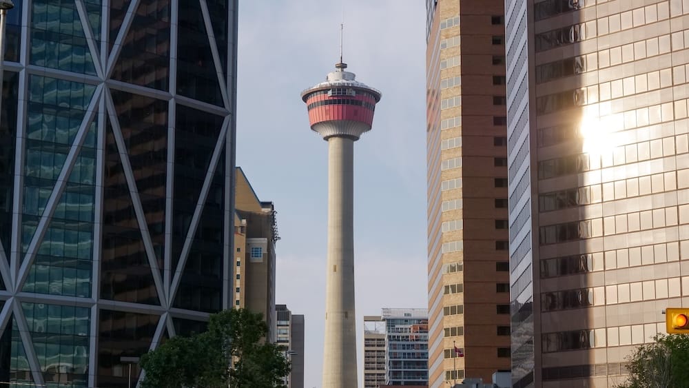Calgary Tower enmarcada por edificios de oficinas del centro de Calgary, Alberta, Canadá Calgary Tower se eleva entre modernos edificios de oficinas en el centro de Calgary, Alberta, Canadá, mientras la luz cálida del atardecer se refleja en la fachada de vidrio de una torre cercana.