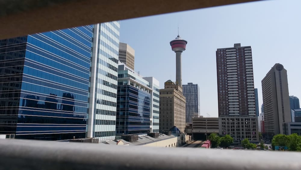 Vista de la Calgary Tower enmarcada a través de la baranda, High Park, Calgary, Alberta, Canadá La Calgary Tower y los rascacielos del centro que la rodean, enmarcados entre los bordes de una baranda en la terraza de High Park en Calgary, Alberta, Canadá, con copas de árboles verdes visibles por debajo de la línea de edificios.