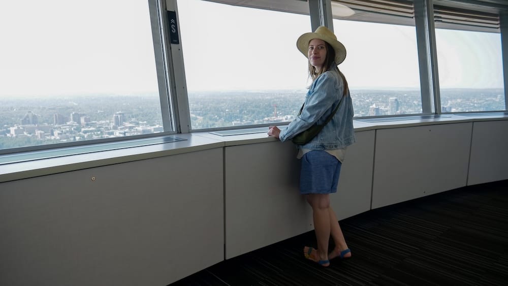 Calgary Tower Observation Deck in Alberta Canada with Audrey Bergner Looking Across the City Skyline Audrey Bergner stands beside the windows inside Calgary Tower in Calgary, Alberta, Canada, looking out across the city from the observation level with the urban landscape stretching into the distance.