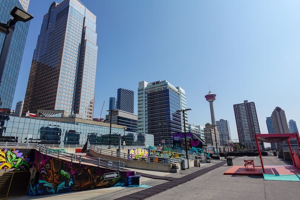 Vista del horizonte desde la terraza de High Park, Calgary, Alberta, Canadá La Calgary Tower y los rascacielos del centro vistos desde la terraza de High Park en Calgary, Alberta, Canadá, con murales llenos de grafitis en las rampas y un espacio colorido para sentarse en primer plano.