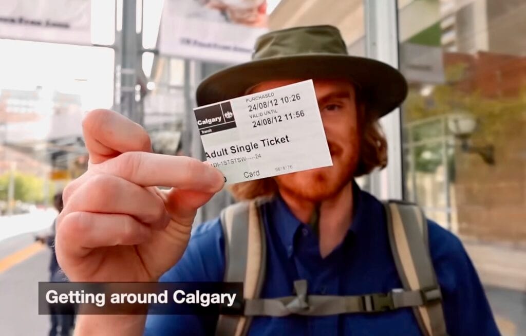 Calgary Transit CTrain Ticket Alberta Canada Public Transport to Heritage Park with Samuel Jeffery Journey Samuel Jeffery holds an adult Calgary Transit ticket toward the camera while waiting for a CTrain in Calgary, Alberta, Canada, with a backpack and station platform behind him.