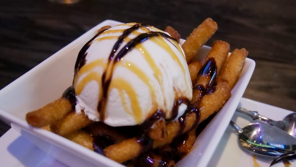 Primer plano macro de la Dessert Poutine en The Canadian Icehouse de Edmonton, Alberta, con bastones de masa frita cubiertos de canela y azúcar, helado de vainilla, chocolate y caramelo.