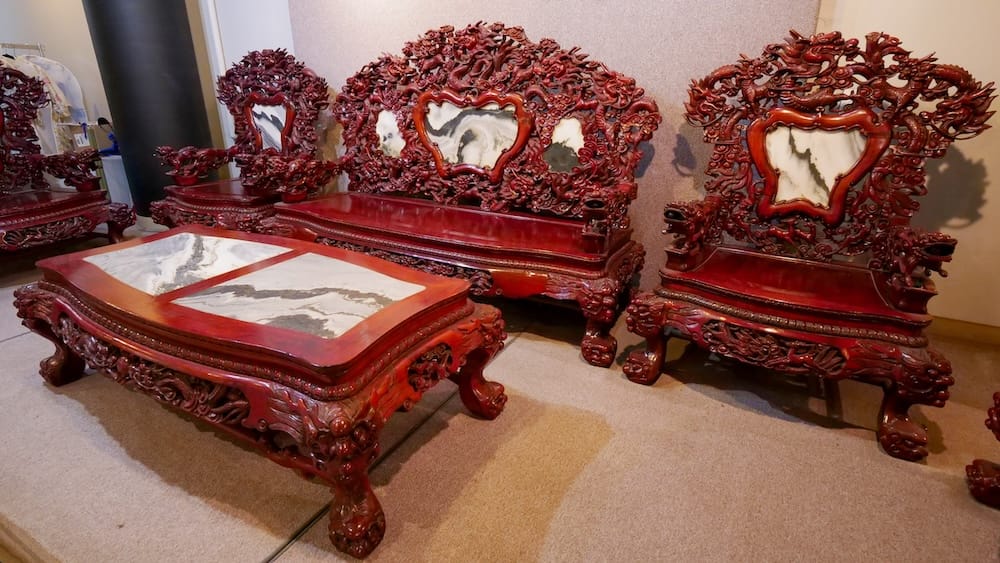 An ornately carved dark red mahogany furniture set with dragon motifs and inlaid marble panels, part of a Qing Dynasty-style dining set on display in the Chinese Artifacts Museum in Calgary, Alberta, Canada.