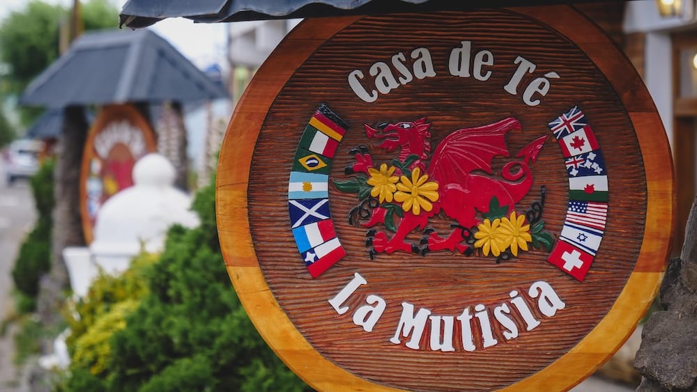 Casa de Té La Mutisia sign in Trevelin Patagonia featuring the Welsh dragon and international flags, representing the fusion of Welsh heritage and global influences in modern tea houses in Argentina’s Chubut region