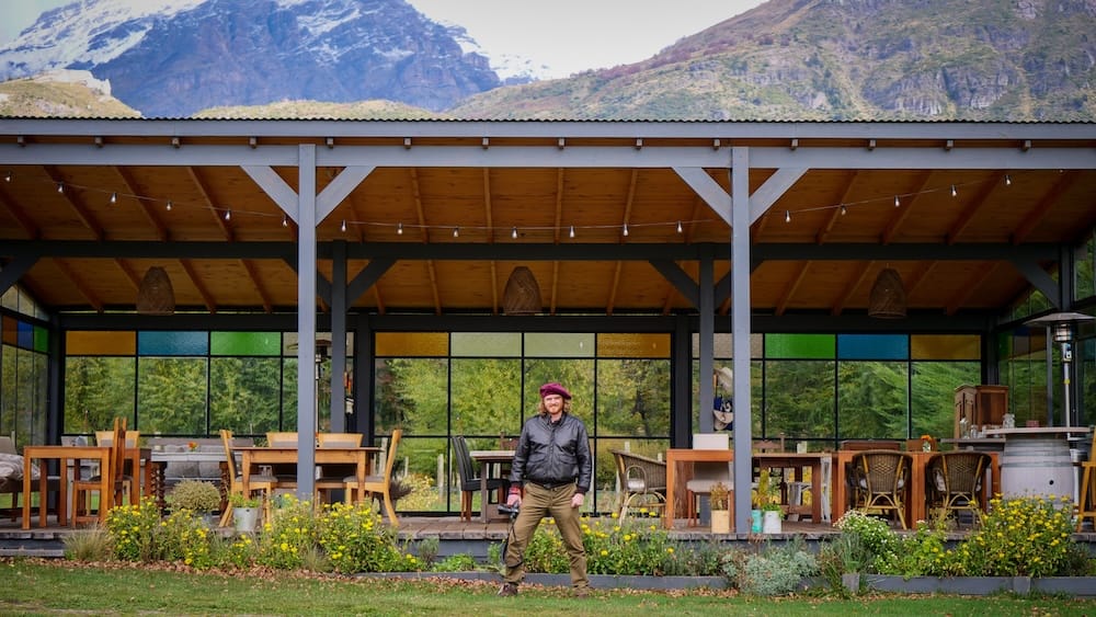 Samuel Jeffery outside Casa Yagüe in Trevelin, Chubut, Patagonia, Argentina, with a mountain backdrop Samuel Jeffery stands outside the Casa Yagüe vineyard building in Trevelin, Chubut, Patagonia, Argentina, framed by an open terrace, garden plantings and rugged mountains rising behind the property.