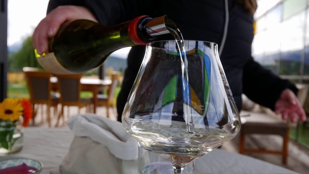 White wine being poured at Casa Yagüe vineyard in Trevelin, Chubut, Patagonia, Argentina White wine is poured into a large stemmed glass during a vineyard visit at Casa Yagüe in Trevelin, Chubut, Patagonia, Argentina, with a rustic tasting area and softly blurred mountain scenery in the background.