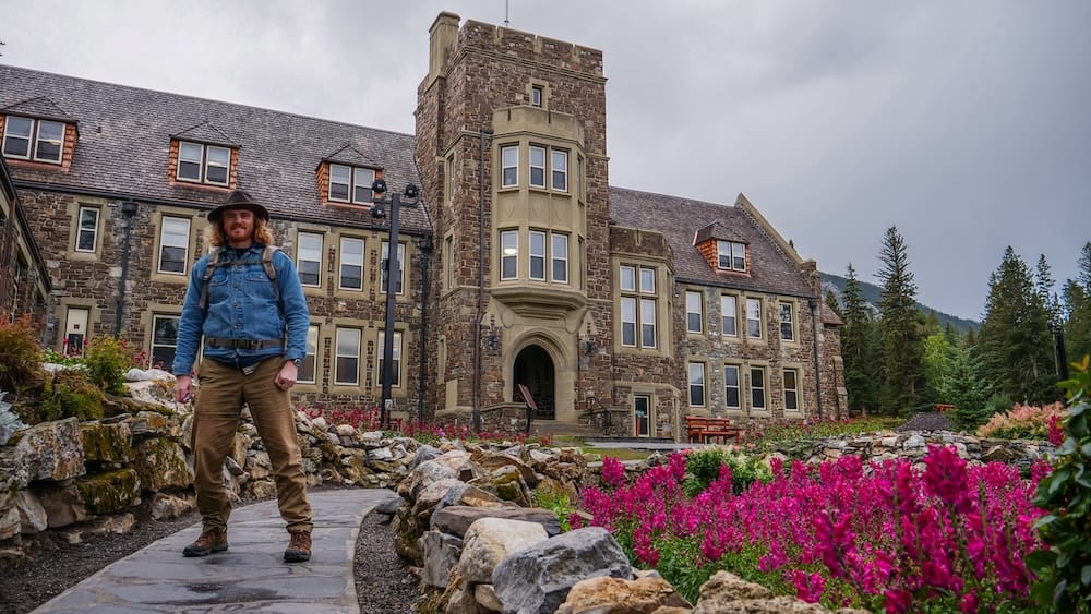 Samuel Jeffery at Cascades of Time Garden in Banff, Alberta, Canada, beside the Parks Canada Administration Building Samuel Jeffery standing among stone paths and bright flower beds at Cascades of Time Garden in Banff, Alberta, Canada, with the historic Parks Canada Administration Building rising behind him.