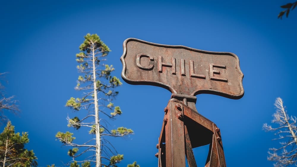 Chile border sign in Lago Puelo Patagonia near Argentina crossing point Rusted Chile border sign at Lago Puelo in Patagonia marking entry from Argentina to Chile with forest trees and blue sky in the background