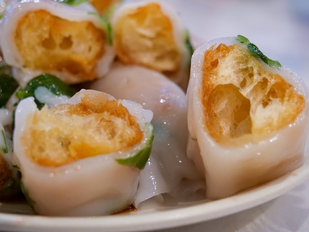 Close-up of a dim sum rice roll with fried dough at a restaurant in Calgary Chinatown, Alberta, Canada, showing the soft rice noodle wrapper around the crisp golden centre on a sauce-lined plate.