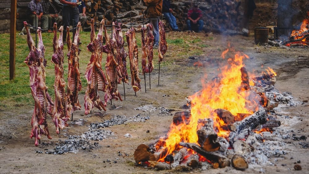 Traditional Argentine asado with whole lamb cooking over an open fire in Cholila Patagonia Argentina showing rural cooking traditions in the Andes region and the cultural food experiences found in mountain Patagonia.