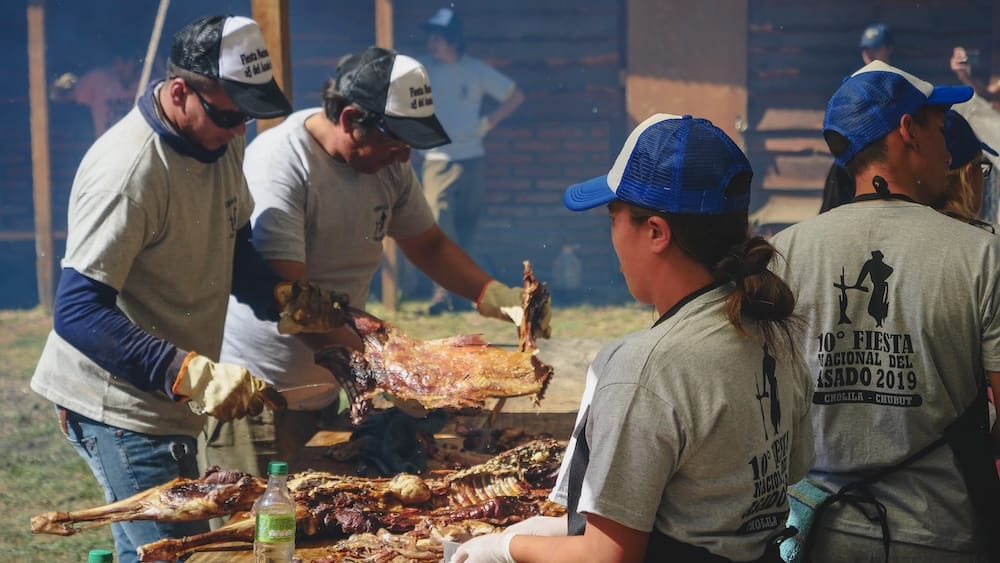 Butchers carving roasted lamb at Fiesta Nacional del Asado in Cholila Patagonia Argentina, showcasing traditional Patagonian barbecue culture and communal cooking practices.
