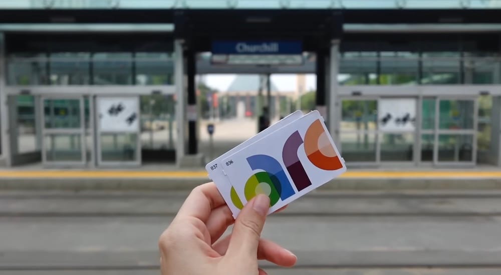 Tarjetas Arc frente a Churchill LRT Station, en el centro de Edmonton, Alberta, Canadá Una mano sostiene dos tarjetas Arc frente a Churchill LRT Station, en el centro de Edmonton, Alberta, Canadá, con la entrada, el borde del andén y las puertas de vidrio desenfocados al fondo.