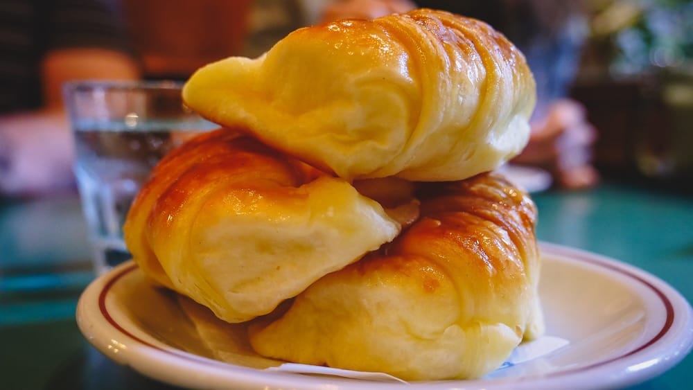 Medialunas clásicas apiladas en un plato blanco en un café patagónico, mostrando la cobertura brillosa de almíbar y la masa suave que hacen de estas facturas el desayuno infaltable de los argentinos antes de ir a la montaña.
