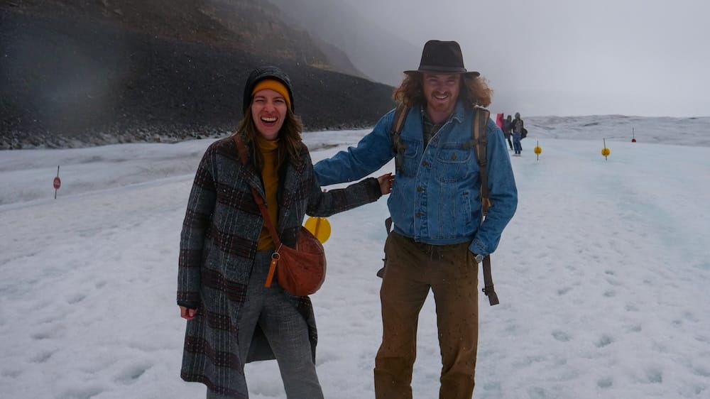 Audrey Bergner and Samuel Jeffery standing together on the snowy Columbia Icefield in Alberta, Canada, surrounded by mist, glacial terrain and dark Rocky Mountain slopes.