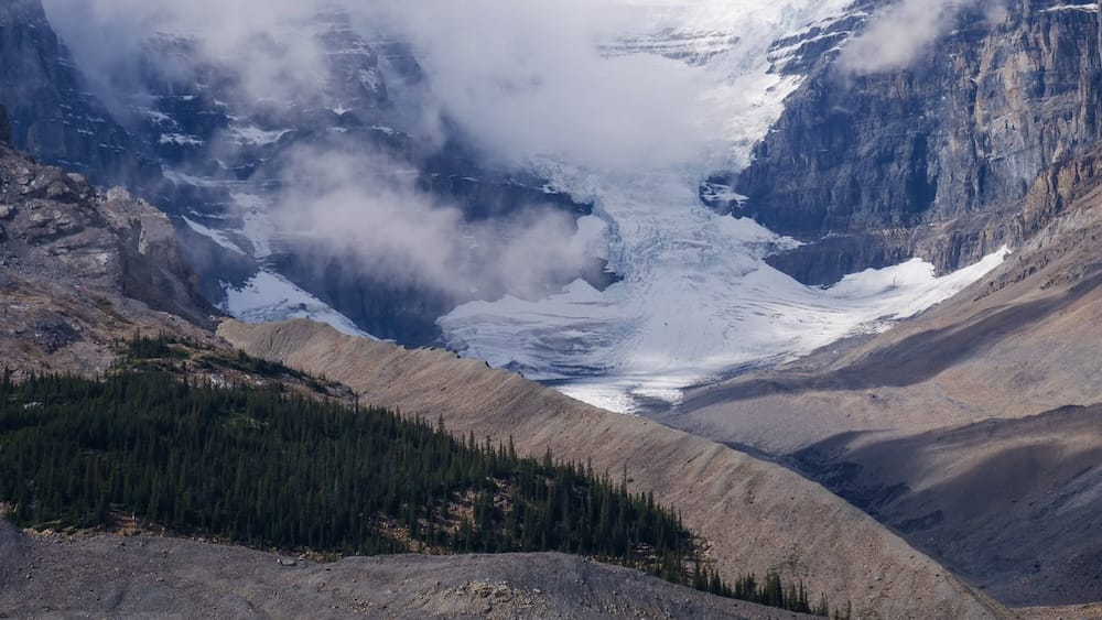 Columbia Icefield Alberta Canada Glacier and Mountain View With Low Cloud Along the Icefields Parkway Columbia Icefield in Alberta, Canada, with glacier ice descending between steep rocky mountain walls, low cloud drifting across the ice and dark evergreen forest below.
