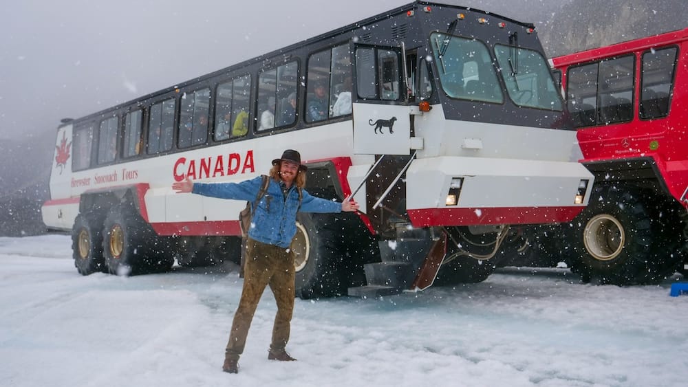 Columbia Icefield near Athabasca Glacier, Alberta, Canada - Ice Explorer glacier tour in snowy weather with Samuel Jeffery Samuel Jeffery stands on the snow beside an Ice Explorer at the Columbia Icefield near Athabasca Glacier in Alberta, Canada, with falling snow, low visibility and another glacier vehicle behind him.