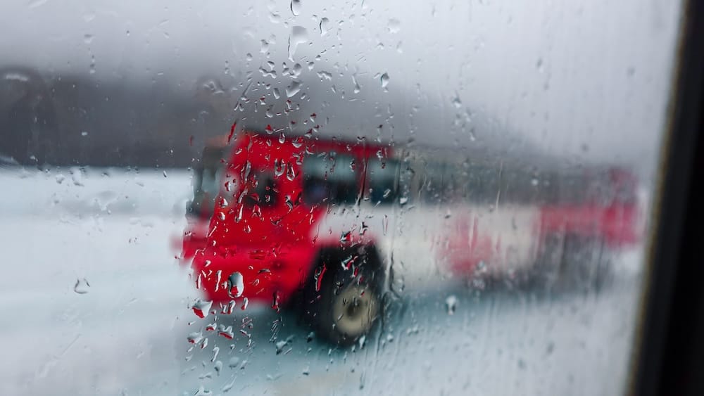 Un vehículo rojo Ice Explorer se ve a través de una ventana con gotas de lluvia y condensación en Columbia Icefield, Alberta, Canadá, con terreno glaciar nevado y nubes bajas desenfocadas al fondo.