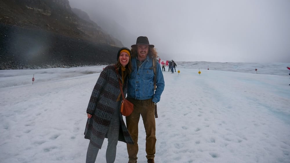 Athabasca Glacier at Columbia Icefield, Jasper National Park, Alberta, Canada with Samuel Jeffery and Audrey Bergner Audrey Bergner and Samuel Jeffery standing together on the snowy Athabasca Glacier at Columbia Icefield in Jasper National Park, Alberta, Canada, with fog and steep dark mountain slopes behind them.