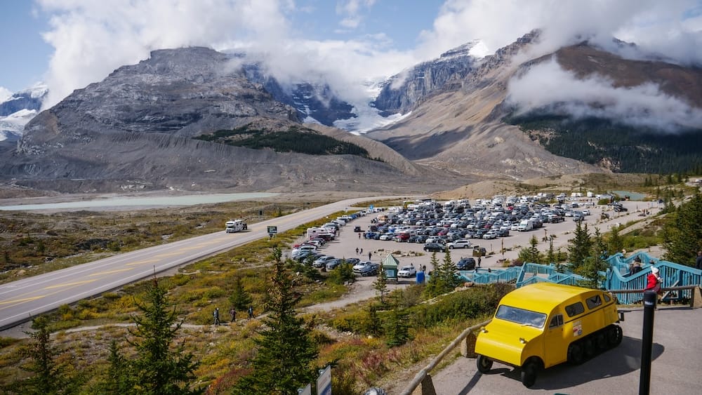 El estacionamiento del Columbia Icefield Discovery Centre bajo cielo despejado — Alberta, Canadá El estacionamiento del Columbia Icefield Discovery Centre bajo un cielo azul despejado, con el glaciar Athabasca y las montañas circundantes visibles detrás, Alberta, Canadá.