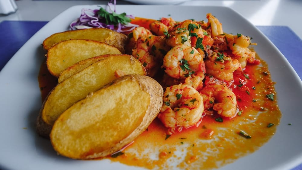 Patagonian shrimp with roasted potatoes served in Comodoro Rivadavia, Chubut, Argentina, showcasing langostinos in a rich tomato and herb sauce, a staple of Atlantic coastal cuisine known for bold flavors and fresh seafood traditions.