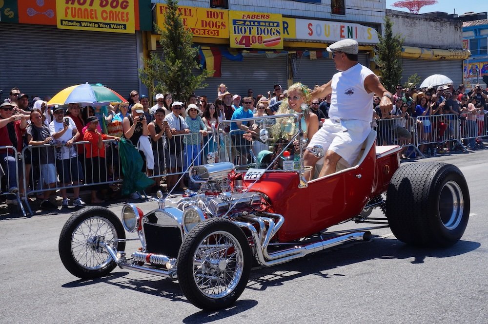 Coney Island man standing up on vintage car 