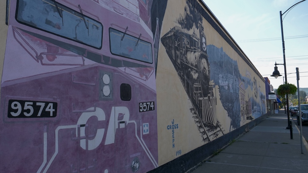 Downtown Cranbrook, BC mural wall featuring a large painted Canadian Pacific Railway locomotive and historic town scenes along a sidewalk, showcasing the city’s railway heritage and colorful public art in the heart of downtown.