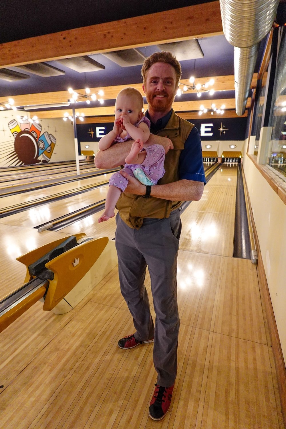 Cranbrook BC bowling lanes at Encore Brewing during a family-friendly visit, with Nomadic Samuel holding baby Aurelia while she happily sings and explores the space, capturing a joyful moment that shows how bowling and pizza can still work for parents traveling with a baby.