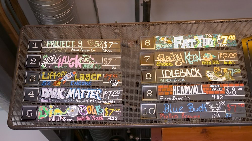 Cranbrook, British Columbia craft beer menu at Fire Hall Kitchen & Tap showcasing the first ten BC local beers on tap, including lagers, IPAs, pale ales, and wheat beers from regional breweries, displayed on a colorful chalkboard menu highlighting the restaurant’s strong focus on local British Columbia brews.
