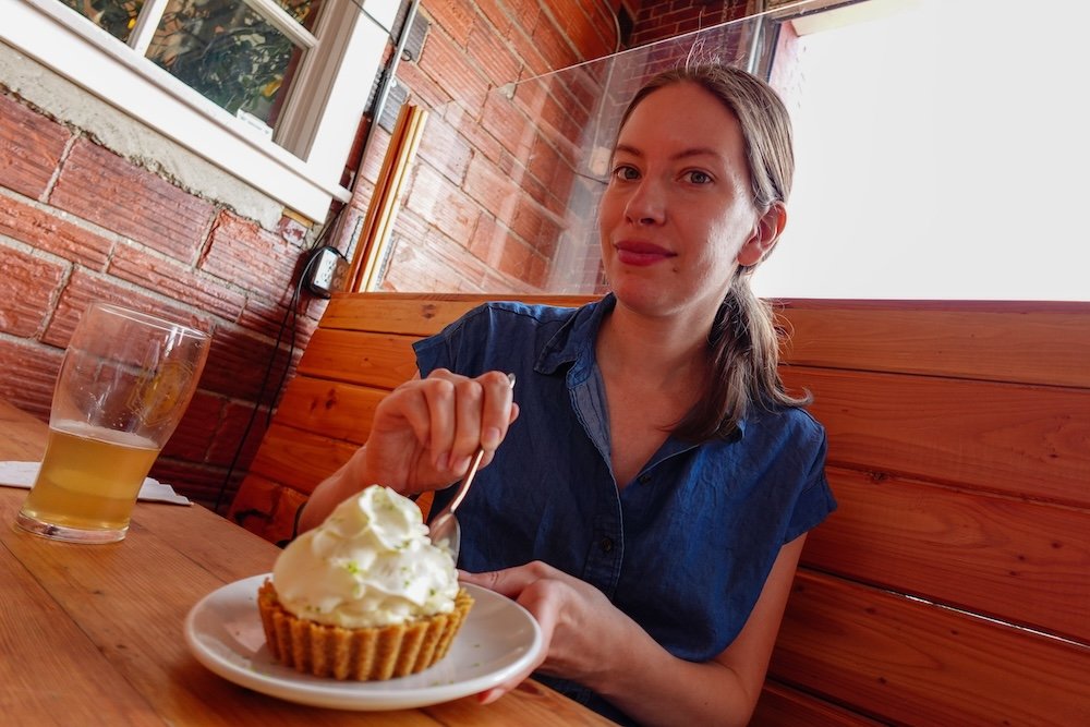 Cranbrook, BC at The Fire Hall Kitchen & Tap shows Audrey Bergner enjoying a slice of key lime pie topped with whipped cream, capturing a relaxed dessert moment inside the historic fire hall restaurant during a casual meal stop while exploring town.

