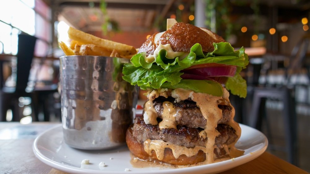 Cranbrook, British Columbia gourmet burger at Fire Hall Kitchen & Tap featuring a towering double beef patty topped with goat cheese, avocado, bacon, and house sauce, served with crispy fries inside one of the city’s most iconic restaurants.