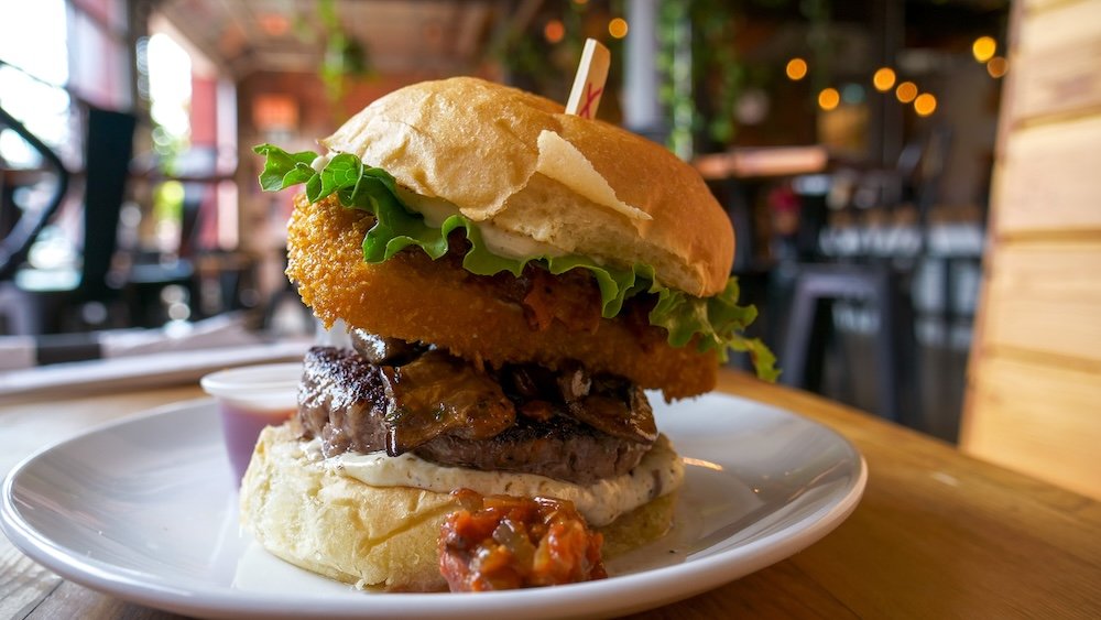 Cranbrook, British Columbia gourmet burger at Fire Hall Kitchen & Tap, featuring a thick beef patty topped with crispy onion rings, lettuce, house sauce, and a toasted bun, served as one of the standout burger options in downtown Cranbrook.