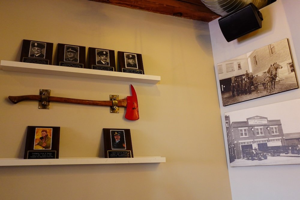 Cranbrook, British Columbia interior of Fire Hall Kitchen & Tap showcasing preserved historic fire hall features, including original firefighter plaques, archival photographs, and mounted fire equipment that highlight the building’s heritage dating back to its construction in 1929.

