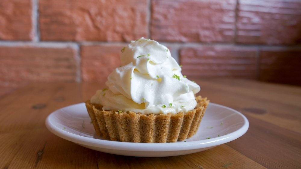 Cranbrook, British Columbia: a slice of legendary key lime pie served at Fire Hall Kitchen & Tap, featuring a buttery graham crust and tall swirl of whipped cream, photographed against the restaurant’s rustic brick interior.