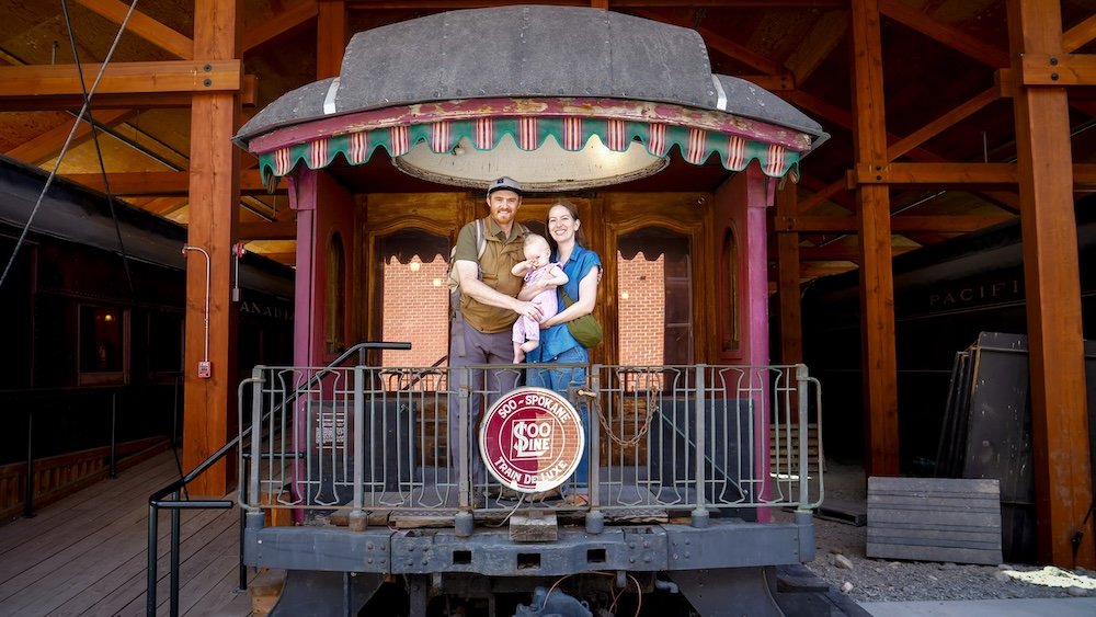 Cranbrook, British Columbia, showcasing historic railway carriages as Nomadic Samuel and Audrey Bergner hold baby Aurelia while exploring restored trains, highlighting Cranbrook’s rail history, family-friendly museums, and why this heritage stop makes an engaging and easy day trip from Fernie.