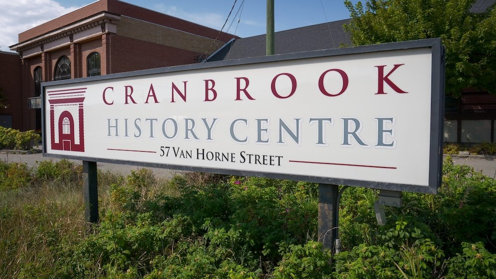 Cranbrook History Centre museum sign Sign for the Cranbrook History Centre in Cranbrook, British Columbia, displayed in front of the brick museum building, showing the entrance address on Van Horne Street and surrounded by greenery under a bright summer sky.