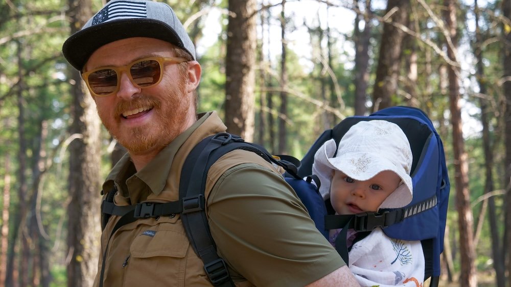 Family-friendly hiking at Cranbrook Community Forest in BC with Nomadic Samuel and baby Aurelia Cranbrook Community Forest in British Columbia during a family-friendly hike, with Nomadic Samuel carrying baby Aurelia in a backpack carrier while walking through tall pine forest, showing how easy and rewarding outdoor adventures are with a baby in Cranbrook.