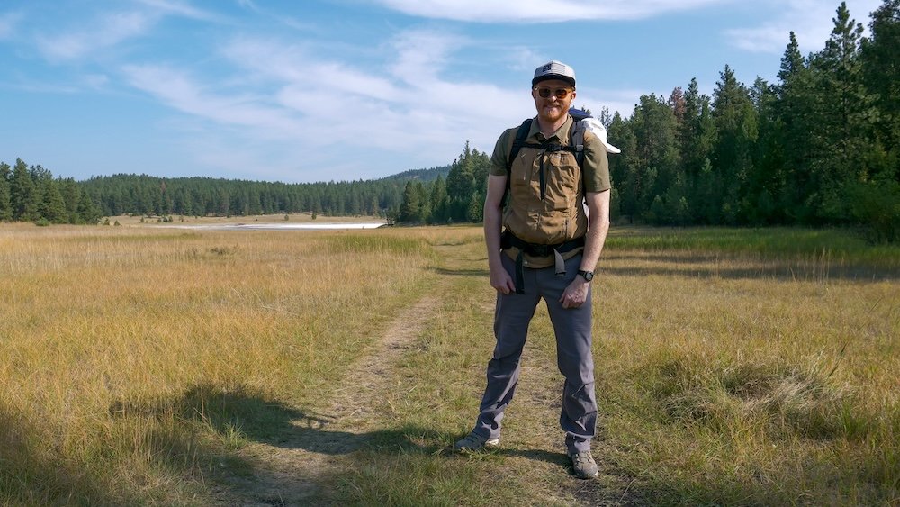 Cranbrook Community Forest meadow trail near Cranbrook, BC, with wide open grassland and forest edges as Nomadic Samuel hikes while carrying baby Aurelia, showing how relaxed and scenic this close-to-town forest is for an easy family day trip.