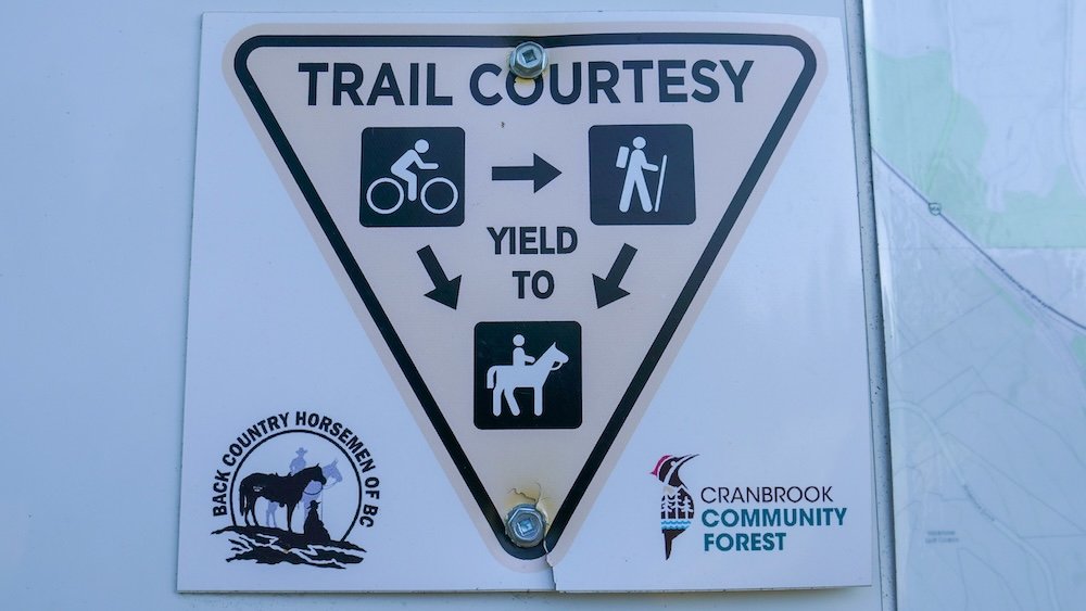 Cranbrook Community Forest trail courtesy sign explaining right-of-way: cyclists yield to hikers, and both cyclists and hikers yield to horseback riders, helping visitors share multi-use trails safely in Cranbrook, BC.
