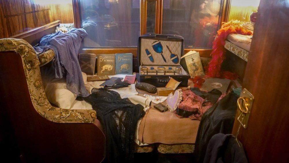 Historic train sleeping compartment on the guided train tour at the Cranbrook History Centre in Cranbrook, British Columbia, displaying period luggage, books, clothing, and personal items that recreate everyday life aboard early Canadian rail travel.