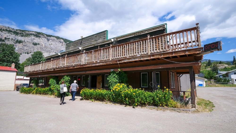 Crowsnest Pass, Alberta mountain town streetscape showing a rustic roadside building and surrounding scenery, illustrating how travelers can base themselves in the Crowsnest Pass and enjoy an easy, scenic day trip drive to Fernie, British Columbia.