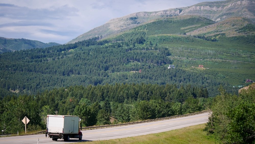 Driving through Crowsnest Pass near Bellevue, Alberta, with Highway 3 winding past forested hills and mountain slopes, capturing a scenic stretch of road travelers experience on the drive from Calgary to Fernie through southern Alberta.

