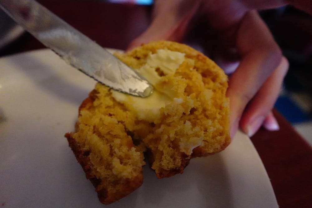 Muffin de Pan de Maíz de DaDeO con Manteca Derretida, Whyte Avenue, Old Strathcona, Edmonton, Alberta, Canadá Primer plano de un muffin tibio de pan de maíz en el restaurante DaDeO en Whyte Avenue en Edmonton, Alberta, Canadá, partido al medio con un cuchillo untando manteca derretida por encima.
