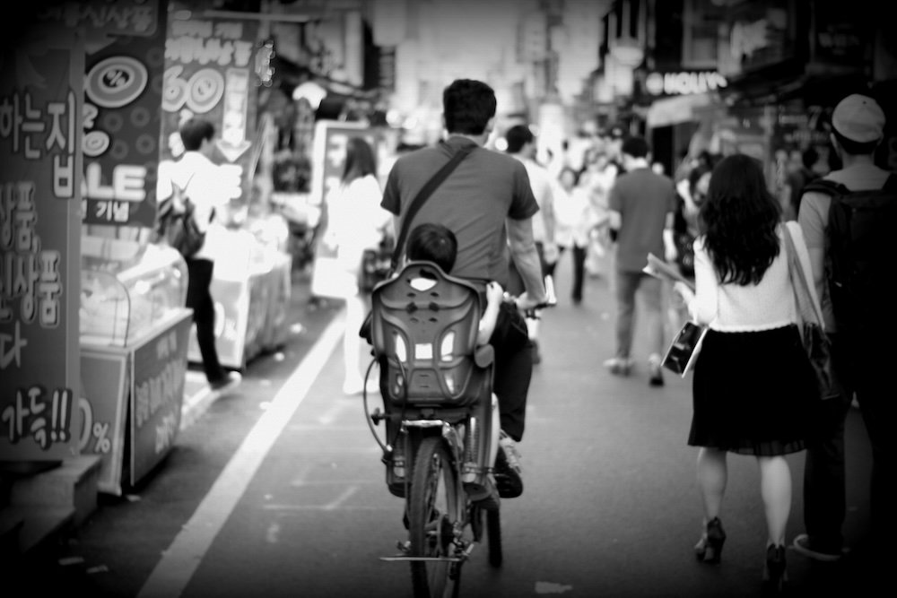 Daejeon street scene with a Korean man riding a bike with his son on the back 