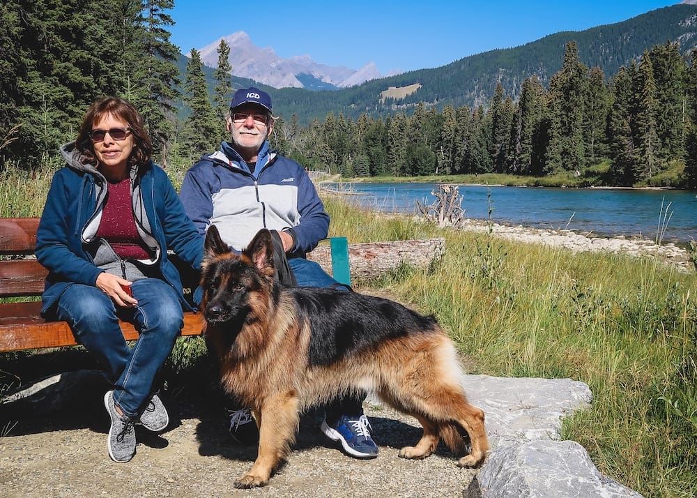 Quiet riverside bench along the Bow River, Banff, Alberta, Canada Daniel and Maria Bergner sit on a riverside bench with their German Shepherd Togo beside them, mountains and a quiet stretch of the Bow River behind them near Banff, Alberta, Canada, with no one else in sight.
