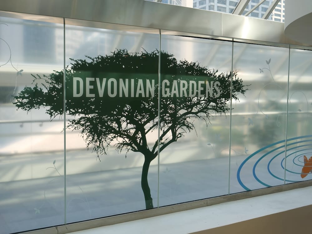 Cartel de Devonian Gardens con un gran gráfico de árbol sobre vidrio dentro de The CORE Shopping Centre en Calgary, Alberta, Canadá, marcando el acceso al jardín interior.