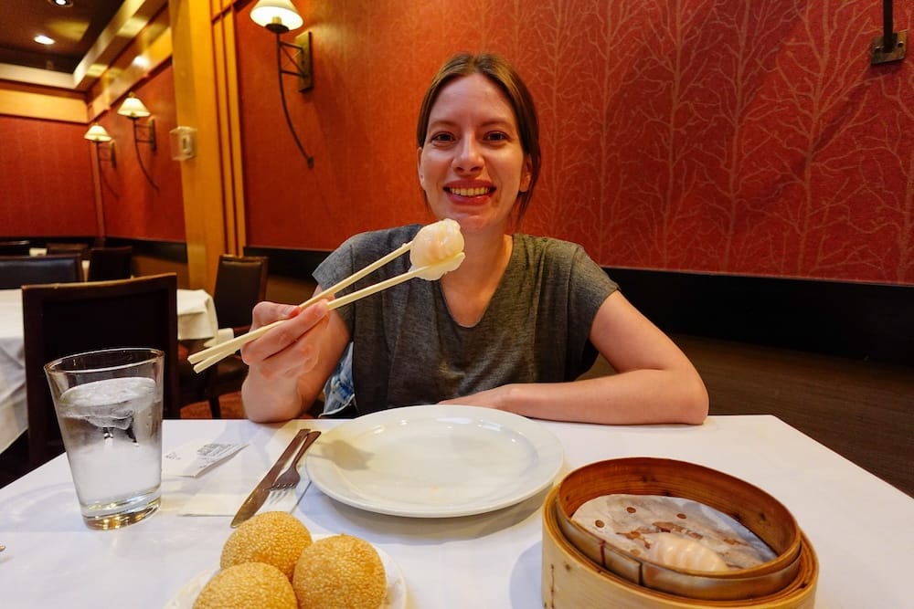 Audrey Bergner eating dim sum in Calgary, Alberta, Canada Audrey Bergner holding chopsticks with a dumpling over a bamboo steamer of dim sum and sesame balls at a Calgary restaurant, Alberta, Canada.