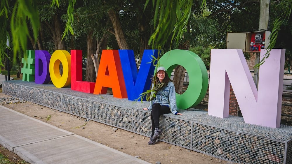Dolavon town sign in the Chubut Valley Patagonia Argentina with Audrey Bergner sitting beside colorful letters representing one of the small Welsh heritage towns in coastal Patagonia known for its tea culture and rural atmosphere.