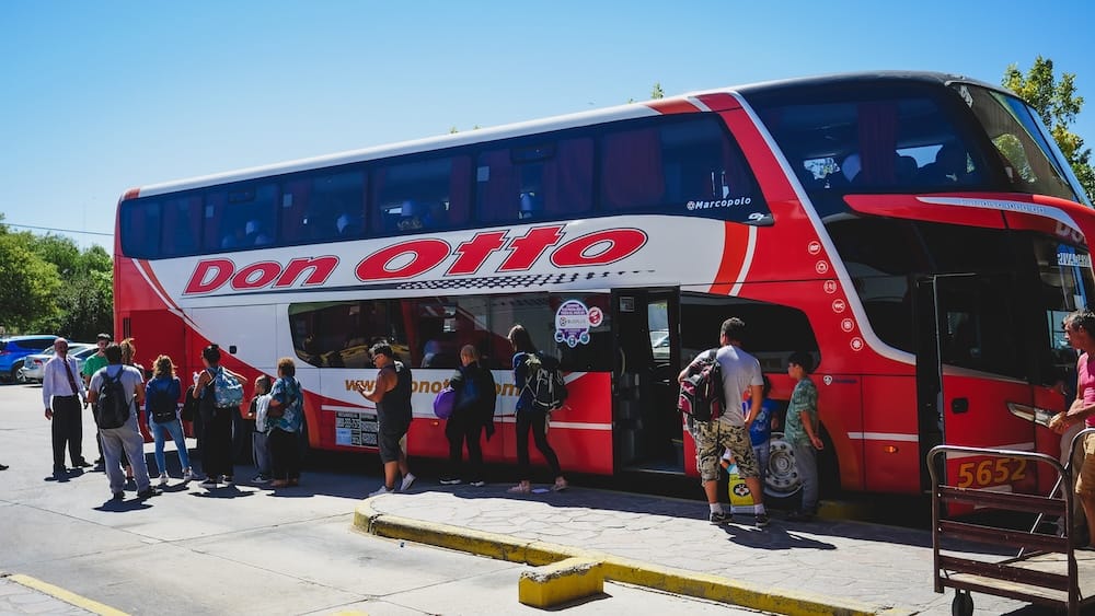 Don Otto Overnight Bus to Puerto Madryn in Patagonia, Argentina, with Passengers Boarding Passengers board a red-and-white Don Otto long-distance coach for an overnight bus journey to Puerto Madryn in Patagonia, Argentina, with luggage and travel bags gathered beside the open doors.