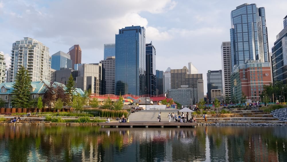Downtown Calgary Alberta Canada Skyline and Waterfront Park with Reflections and Urban Green Space Downtown Calgary skyline reflected in a landscaped pond in Calgary, Alberta, Canada, with modern high-rises, trees, pathways and people gathered around the waterfront on a summer day.